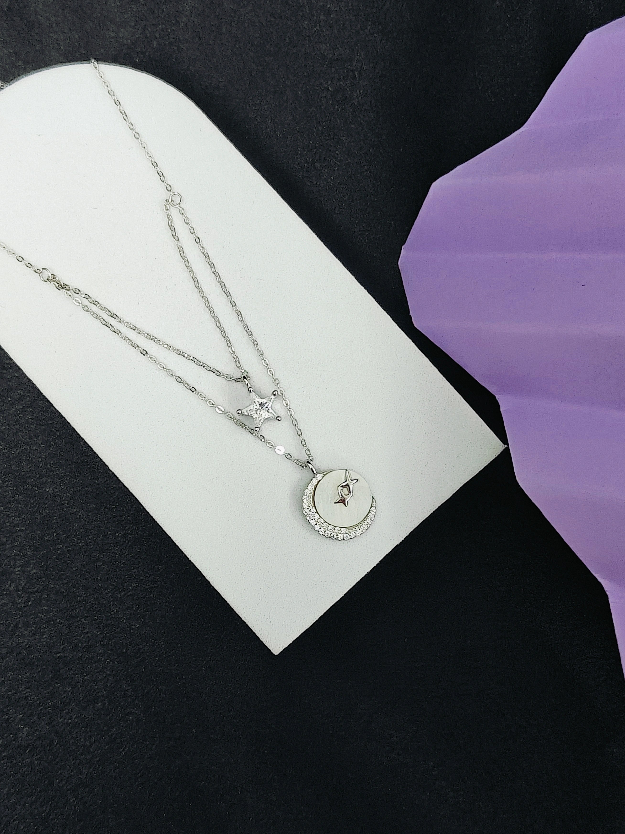 Two silver necklaces on a white card with a purple background